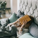 Woman resting in bed holding a book, creating a serene indoor atmosphere perfect for relaxation and leisure.