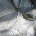A cozy, inviting bed with white linens lit by morning sunlight, creating a restful atmosphere.