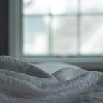 A tranquil bedroom view with a quilted blanket by the window softly lit by morning light, ideal for relaxation themes.